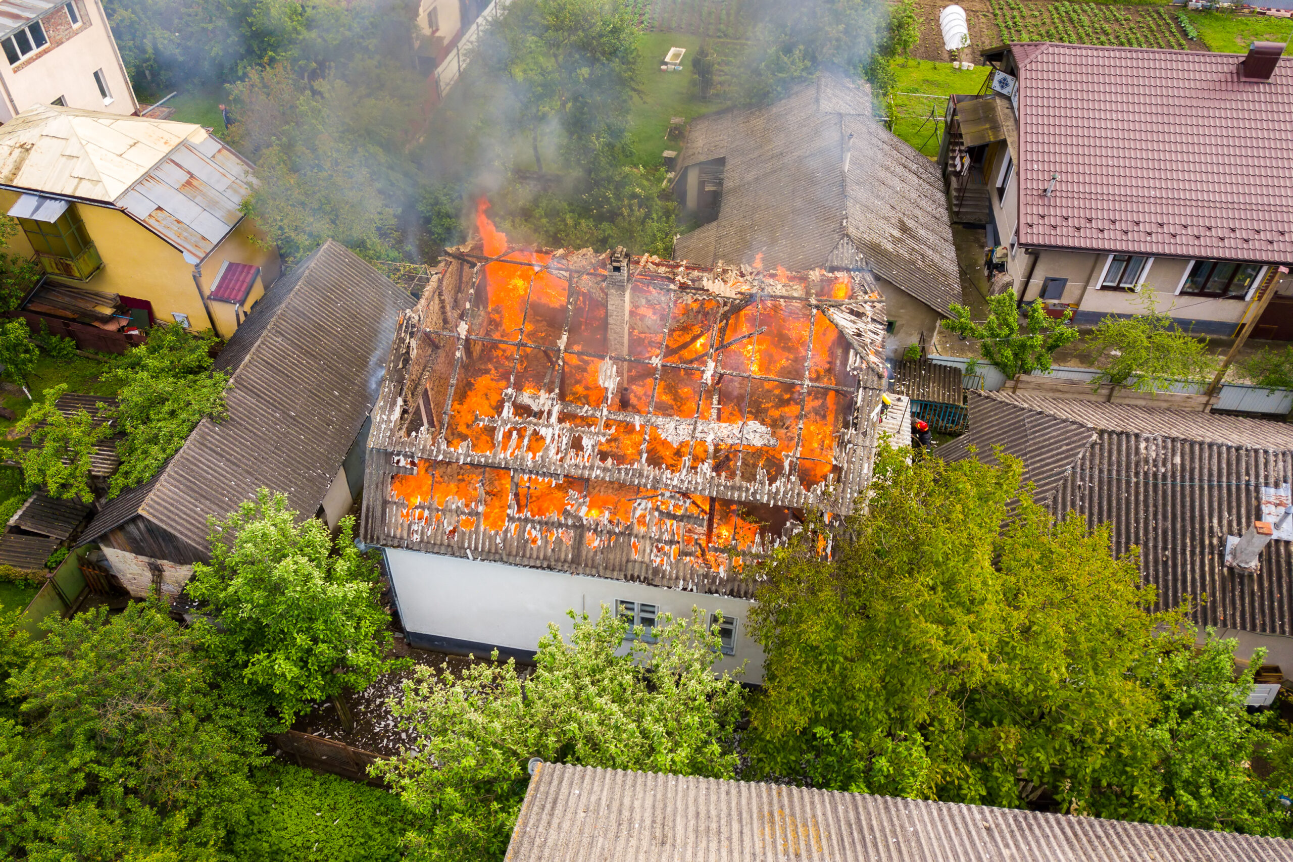 Aerial view of a house on fire with orange flames and white thick smoke.