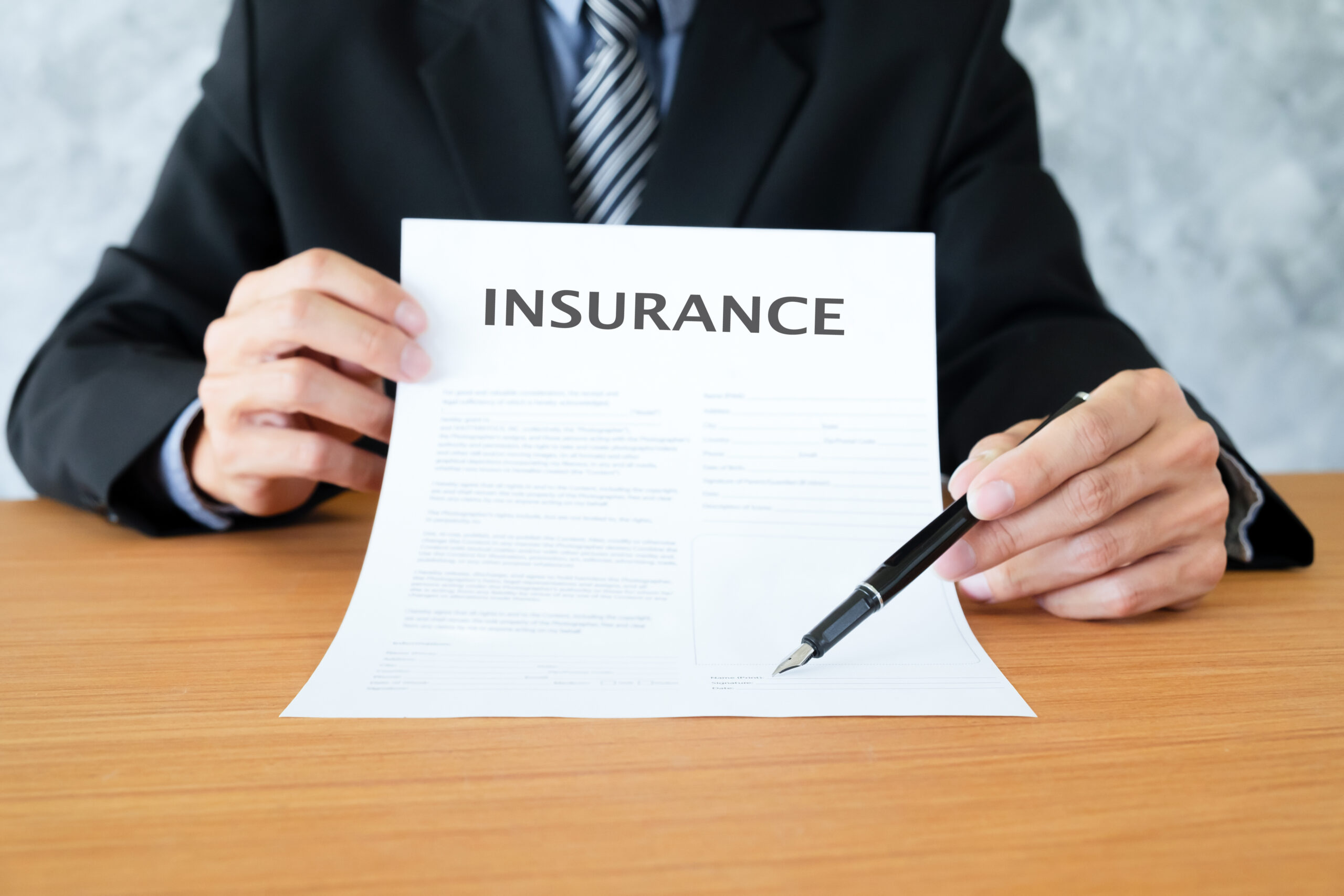A young man in suit in his office showing an insurance policy and pointing with a pen where the policyholder must sign.